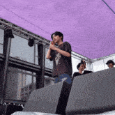 a man stands on a stage under a purple canopy with a microphone