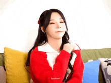 a young woman in a red sweater is sitting on a couch .