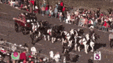 a horse drawn carriage in a parade with a ktla 5 sign in the background