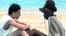 a man and a woman are sitting on the beach and looking at each other