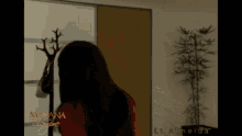 a woman in a red dress is standing in a room with a plant and a coat rack