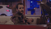 a man in a leather jacket is sitting in a car