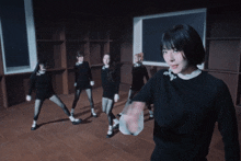a woman in a black sweater stands in front of a group of girls in black dresses