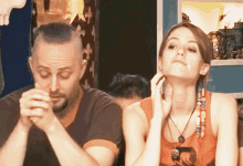 a man and a woman are sitting next to each other and the woman is wearing an orange tank top with the letter o on it