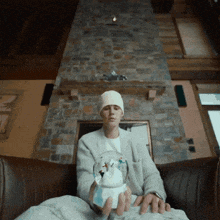 a man sitting on a couch holding a snow globe in front of a fireplace
