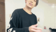 a man in a black sweater is standing in front of a white wall .