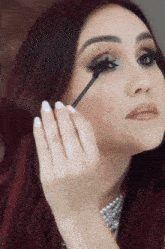 a woman with red hair applying mascara to her eye