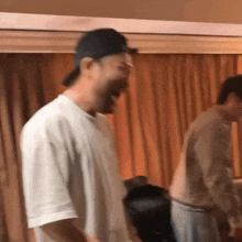 a man wearing a baseball cap is laughing in a room with other men .