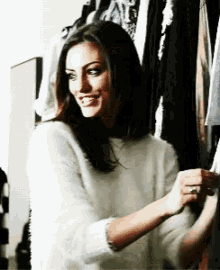 a woman in a white sweater is smiling while standing in front of a closet full of clothes