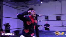 a man in a sweater with hearts on it is in a wrestling ring with # fwlive5