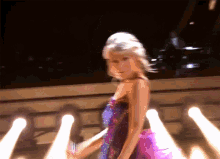 a woman in a purple dress is standing in front of a bunch of lights