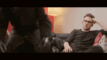 a man wearing glasses is sitting on a couch talking to another man