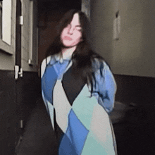 a woman is standing in a hallway wearing a blue and white jacket .
