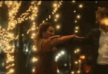 a man in a suit and a woman in a red dress are dancing in front of a string of lights .
