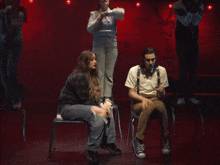 a man in suspenders sits next to a woman in a sweater