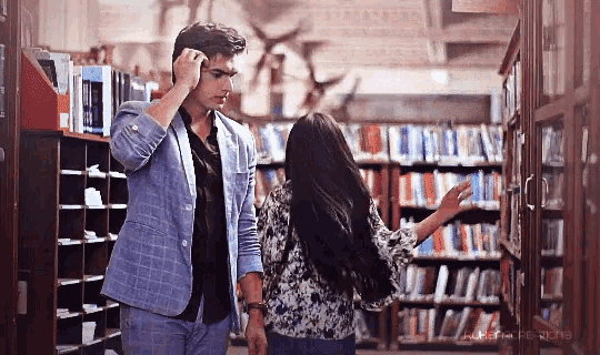 a man and a woman are standing in a library looking at books on shelves