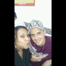 a man wearing a hat with the letter x on it poses with a woman