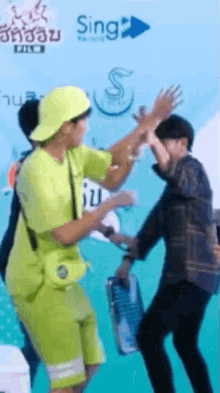a man in a yellow hat is giving a high five to another man .