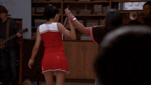 two cheerleaders are dancing in front of a band with a man playing a guitar in the background
