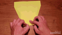 a person 's hands folding a piece of yellow paper with the words made in animotica behind them