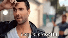 a man in a leather jacket is standing on a city street and talking .