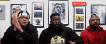 three men are sitting in front of a wall with a youtube subscribe sign