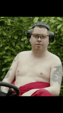 a shirtless man wearing headphones and glasses is sitting in a lawn mower