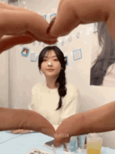 a person is making a heart shape with their fingers in front of a woman 's face