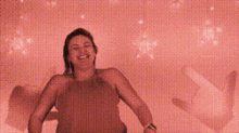 a woman in a red tank top is standing in front of a pink wall with a lot of lights on it .