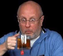 a man with glasses and a beard is holding a cup of tea with a tea bag in it .