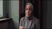a woman wearing a hijab and a grey coat looks at the camera