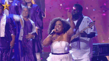 a woman in a white dress sings into a microphone