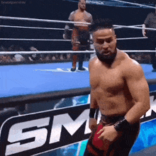 a shirtless wrestler is standing in a wrestling ring with a sm sign behind him