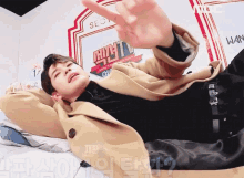 a man in a tan coat is laying on a bed in front of a sign that says mbc