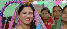 a woman in a pink and blue veil is smiling in front of a group of women .