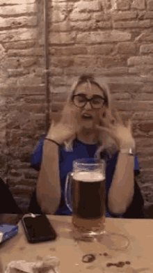 a woman is sitting at a table with a mug of beer and a cell phone .