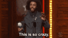a man is holding a trophy in front of a microphone and saying `` this is so crazy . ''
