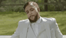 a man with a beard wearing a white suit is sitting on a bench .