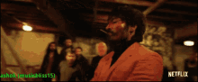 a man in an orange jacket is smoking a cigarette with a netflix logo in the upper right corner