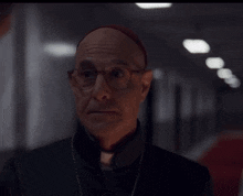 a bald man wearing glasses and a red hat stands in a dark hallway