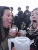 a woman drinking from a pitcher with a straw while another woman drinks from a cup