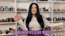 a woman is standing in front of a shelf full of perfume bottles and sending positive vibes .