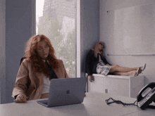 a woman sitting at a desk with an apple laptop and a phone that says ' telephone ' on it