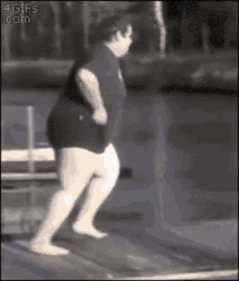 a fat man is jumping off a diving board into a pool .