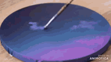 a person is painting a purple and blue circle on a canvas