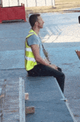 a man wearing a yellow vest sits on a wooden bench