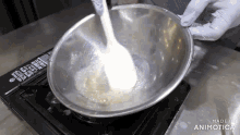 a person is mixing something in a metal bowl on top of a stove with the words made in animatica visible in the corner