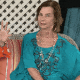 a woman in a blue dress is sitting on a couch waving