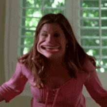 a woman in a pink shirt is making a funny face in front of a window