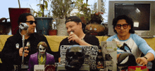 three men are sitting at a table with a sign that says satan on it